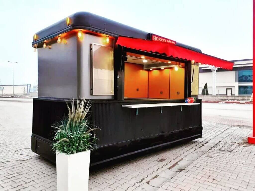 Kırmızı tenteli, servis penceresi açık ve LED aydınlatmalı siyah konteyner kafe