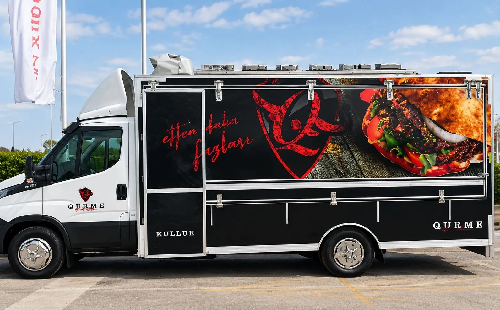 Qurme döner food truck from the side, black and red brand wrap on a white chassis cab, parked outdoors